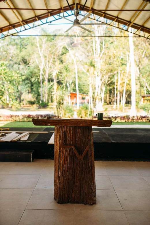 Atril de madera rústica con una taza encima, bajo un techo abierto con ventilador, frente a los árboles
