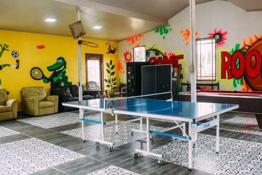 Sala de juegos con mesa de ping-pong, sillones y un mural de colores que dice Game Room