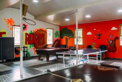 Sala de juegos con mesa de billar y mesa de ping-pong, con paredes rojas pintadas con árboles y animales