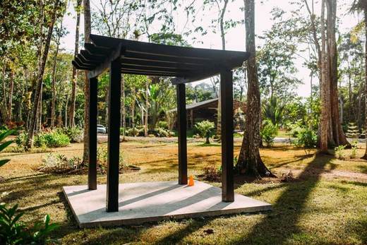 Pérgola de madera oscura sobre una base de concreto, en un jardín con árboles altos